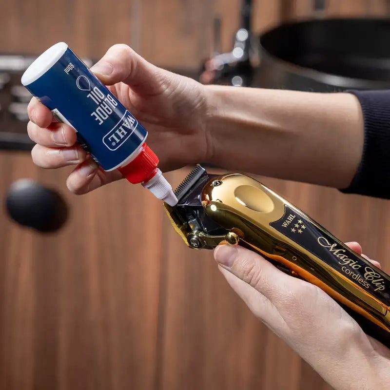 Person applying a blue bottle of gel to a gold and black hair clipper.
