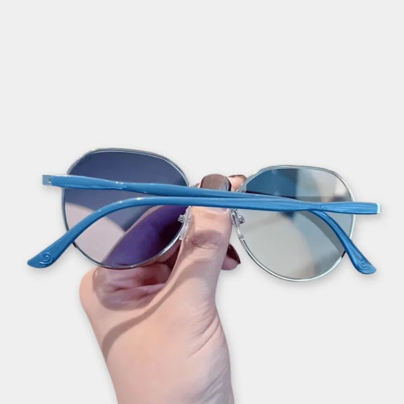 Sunglasses with blue frames held by a hand on a light gray background